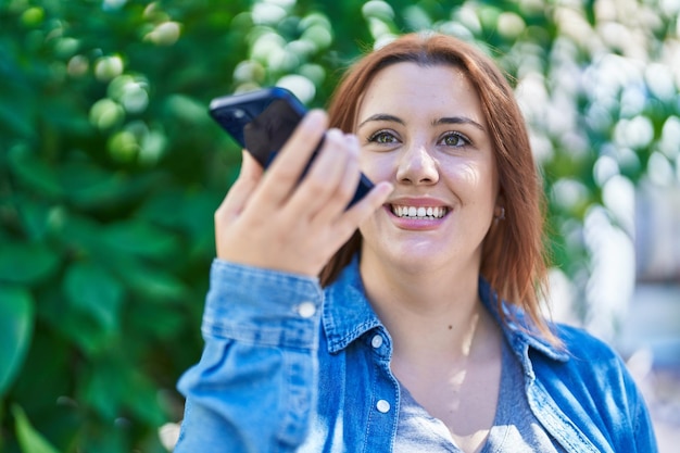 Foto junge schöne frau in übergröße lächelt selbstbewusst und spricht im park auf dem smartphone