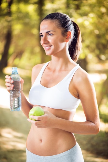 Junge schöne Frau mit Apfel und Wasserflasche in der Natur