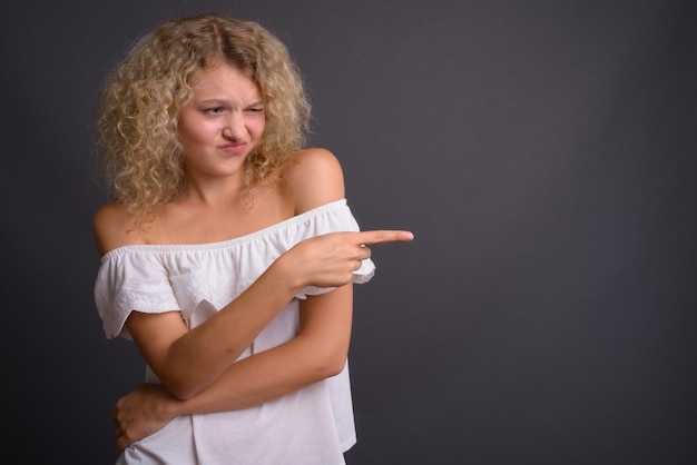 Junge schöne Frau mit blondem lockigem Haar gegen Grau