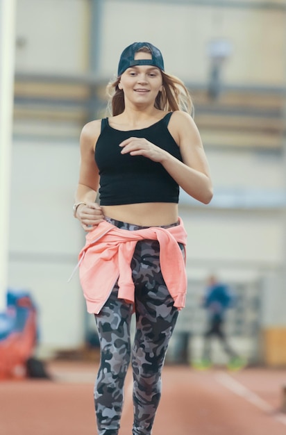 Junge schöne Frau mit blonden Haaren läuft und lächelt in der Sporthalle