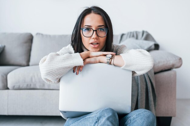 Junge schöne Frau mit Brille, die allein zu Hause mit Laptop sitzt.