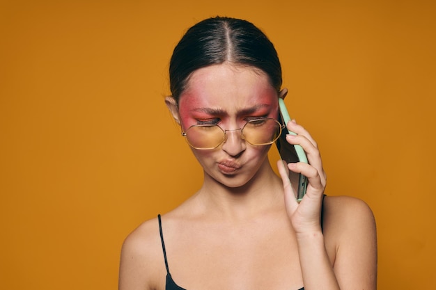 Junge schöne Frau mit Brille, hellem Make-up, die schwarzes Trikot posiert und am Telefon spricht, isolierter Hintergrund unverändert