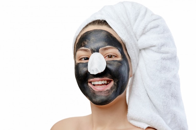 junge schöne Frau mit einem weißen Handtuch auf dem Kopf macht eine Gesichtsmaske, schwarze Maske