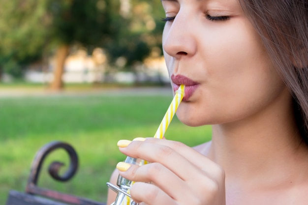 Junge schöne Frau mit einer Flasche frischem Orangensaft genießt ein tolles Wetter im Park