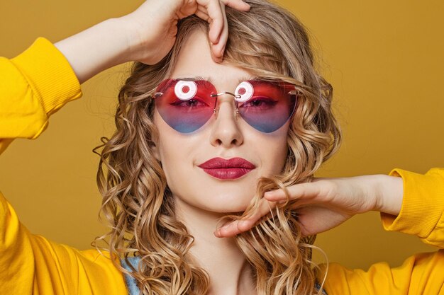 Junge schöne Frau mit einer herzigen Sonnenbrille auf einem leuchtend gelben Hintergrund