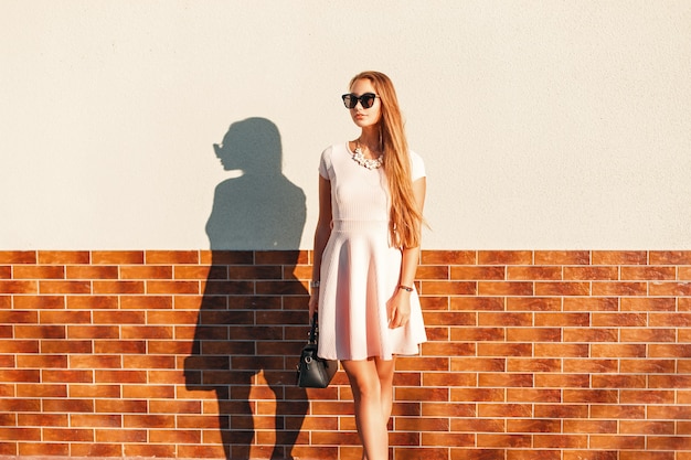 Junge schöne Frau mit einer Tasche in einem rosa Kleid, das nahe der Wand aufwirft