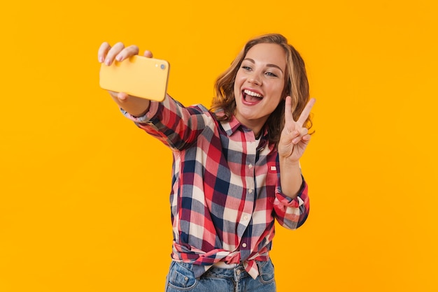 junge schöne Frau mit kariertem Hemd lächelt und macht Selfie auf dem Handy isoliert