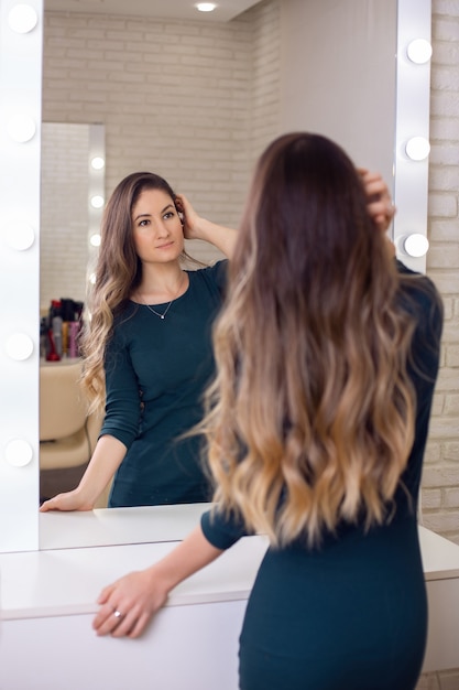 Junge schöne Frau mit langen gesunden brünetten Haaren, die den Spiegel betrachten