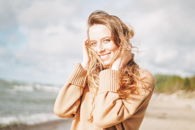 Foto junge schöne frau mit langen haaren in beigem pullover, die das leben am meeresstrand bei sonnenuntergang genießt