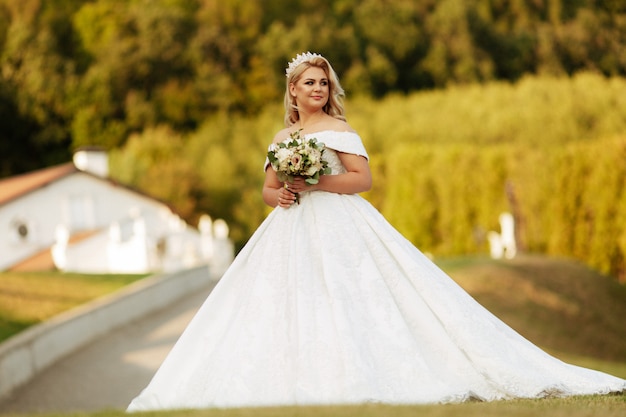 Junge schöne Frau mit langen Haaren und blauen Augen im langen fabelhaften Hochzeitskleid im Herbstpark. Märchenprinzessin im Herbstholz.