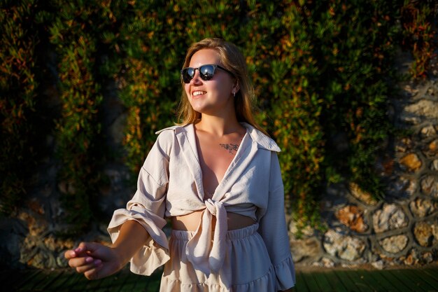 Junge schöne Frau mit Sonnenbrille geht unter der strahlenden Sonne, sie trägt einen beige kurzen Rock und ein Top