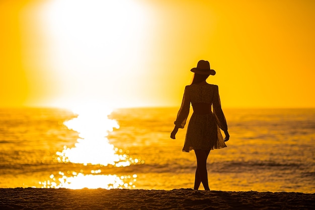 Junge schöne Frau mit Strohhut am Strand bei Sonnenuntergang