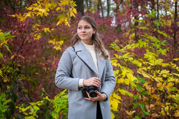 Junge schöne Frau mit Weinlesekamera im schönen Herbstwald. Fotograf fängt die Schönheit des Herbstes ein