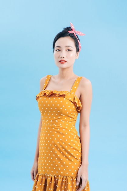 Junge schöne Frau posiert in einem neuen lässigen gelb-weiß gepunkteten Kleid auf einem blauen