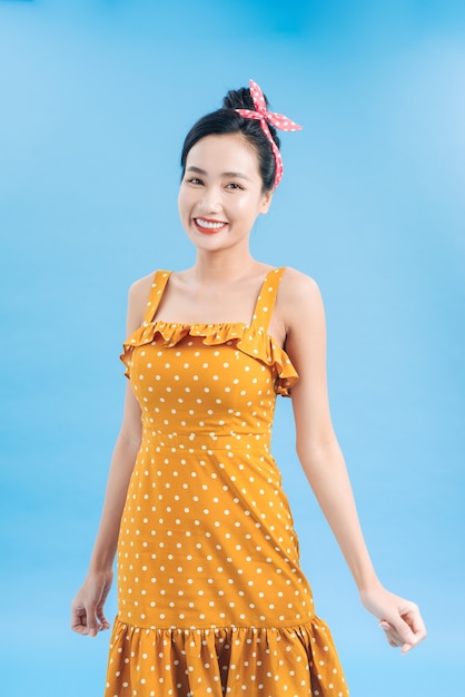 Junge schöne Frau posiert in einem neuen lässigen gelb-weiß gepunkteten Kleid auf einem blauen