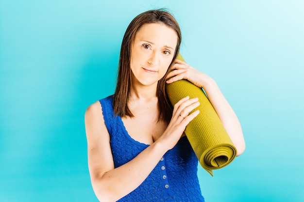 Junge schöne Frau trägt eine Yogamatte auf der Schulter mit blauem Hintergrund gesundes Leben Yoga