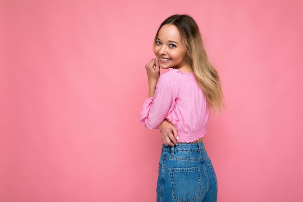 Junge schöne Frau. Trendige Frau im modischen rosa bauchfreien Top. Positives Weibchen zeigt Gesichtsgefühle. Lustiges Modell isoliert auf rosa Hintergrund mit freiem Speicherplatz.