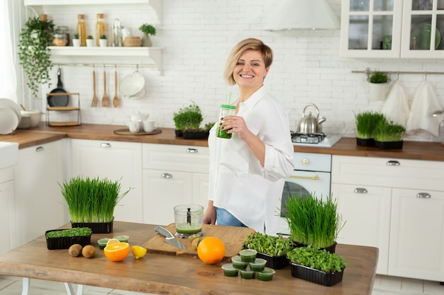 Junge schöne Frau trinkt einen Smoothie aus Weizenkeimsaft und Mikrogrün in der Küche.