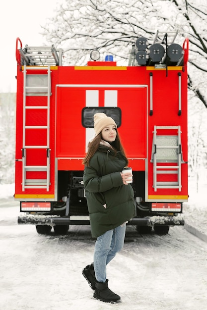 Junge schöne Frau trinkt im Winter Kaffee auf einer Stadtstraße mit einem roten Feuerwehrauto