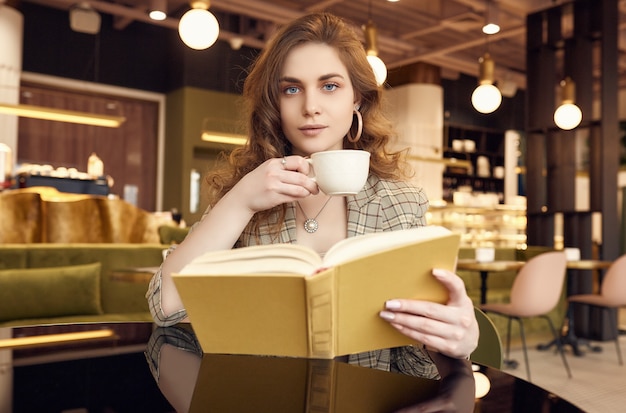 Junge schöne Frau trinkt Kaffee und Lesebuch im Café