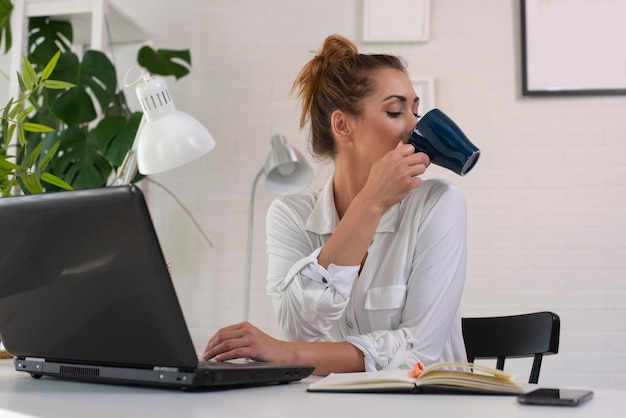 Junge schöne Frau trinkt morgens Kaffee und benutzt Laptop für die Arbeit