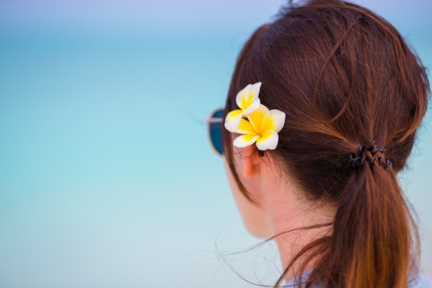 Junge schöne Frau während der tropischen Strandferien. Genießen Sie Ihren Urlaub allein am Strand von Afrika mit Frangipani-Blüten im Haar