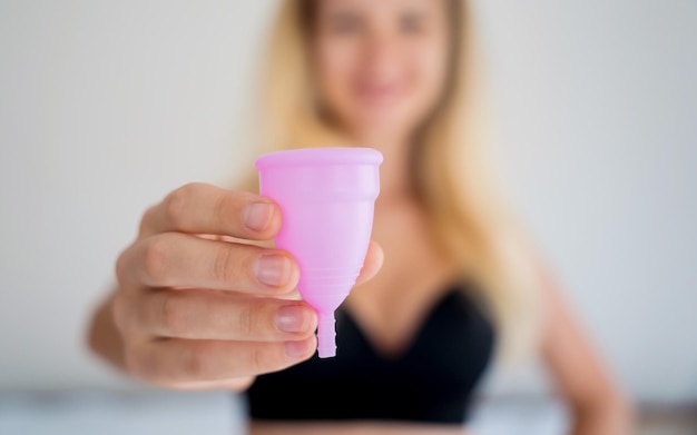 Junge schöne Frau zu Hause hält eine Menstruationstasse in ihren Händen