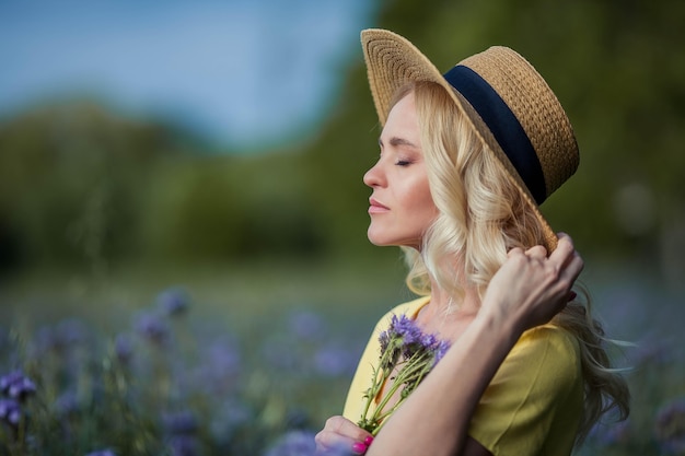 Junge schöne Fraublondine in einem Hut geht durch ein Feld der lila Blumen. Sommer. Frühling.