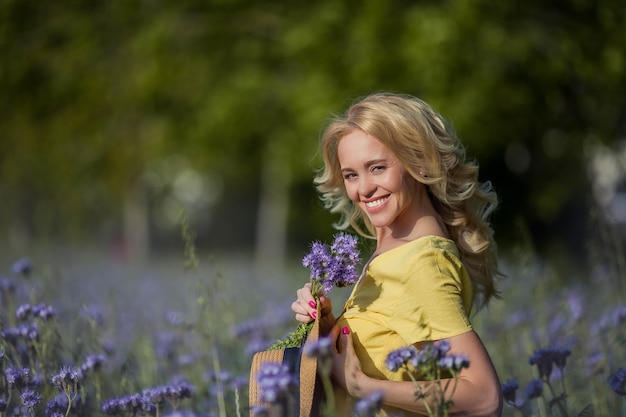 Junge schöne Fraublondine in einem Hut geht durch ein Feld der lila Blumen. Sommer. Frühling.