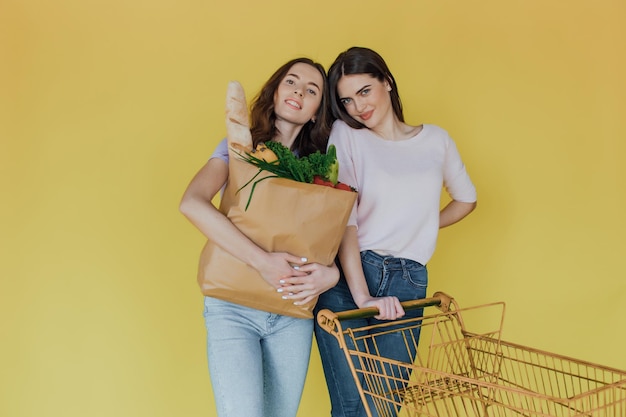 Junge schöne Frauen, die Papiertüten von der Lieferung auf gelbem Hintergrund mitnehmen