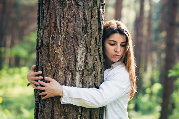 Junge schöne Freiwillige umarmt einen Baum mit Liebe im Wald