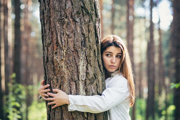 Junge schöne Freiwillige umarmt einen Baum mit Liebe im Wald