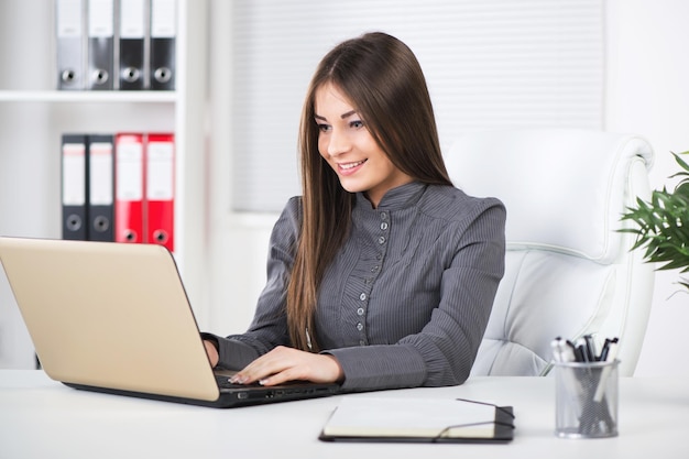 Junge schöne Geschäftsfrau im Büro, sitzend mit Laptop.