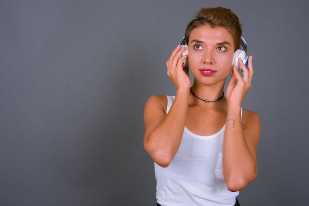 Junge schöne Geschäftsfrau mit blondem Haar, das Musik auf Grau hört