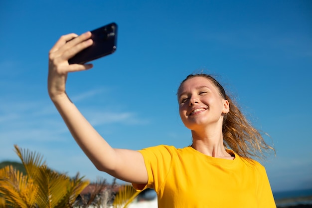 Junge schöne, glückliche Bloggerin macht ein Selfie-Foto von sich selbst mit der Frontkamera in den sozialen Medien