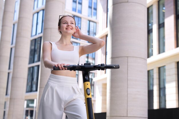 Junge schöne glückliche Frau, die Elektroroller in der Stadt reitet und lächelt Elektrischer Öko-Sharing-Transport