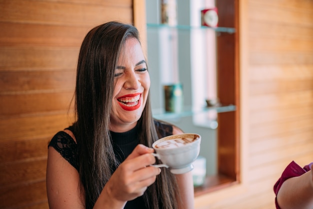 Junge schöne glückliche lateinische Frau, die Cappuccino in einem Straßencafé genießt