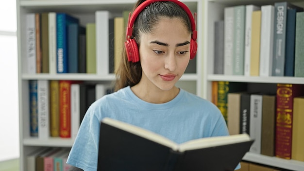 Junge schöne hispanische Studentin liest Buch und hört Musik in der Bibliothek der Universität