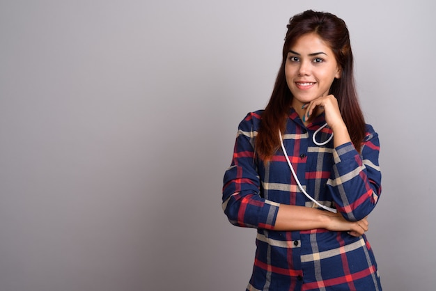 Junge schöne indische Frau, die kariertes Hemd gegen Grau trägt