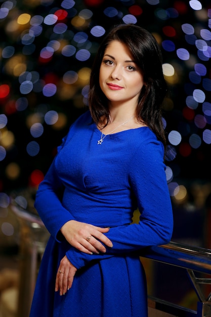 Junge schöne junge schöne Frau im blauen eleganten Abendkleid mit buntem Bokehhintergrund des Weihnachtsfestes