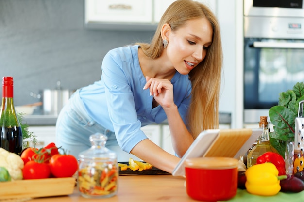 Junge schöne kaukasische Frau, die ihr digitales Tablett in der Küche kocht und verwendet