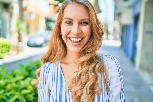 Junge schöne kaukasische Frau mit blonden Haaren lächelt glücklich und fröhlich zu Fuß an einem sonnigen Tag