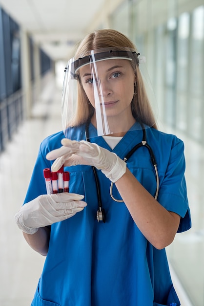 Junge schöne Krankenschwester in Uniform steht im Flur und hält eine Blutprobe. Medizinkonzept