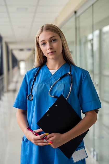 Junge schöne Krankenschwester mit einem Stethoskop um den Hals und einem Tablet in den Händen steht auf dem Flur des Krankenhauses. Medizinkonzept