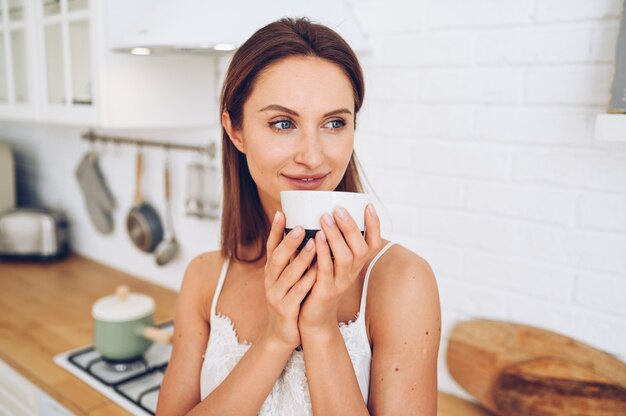 Junge schöne lächelnde Frau, die Morgenkaffee trinkt.