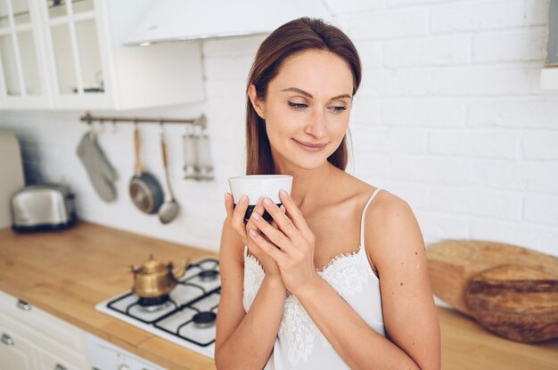 Junge schöne lächelnde Frau, die Morgenkaffee trinkt.