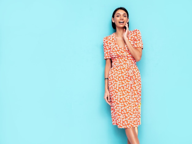 Junge schöne lächelnde Frau im trendigen roten Sommerkleid Sexy sorglose Frau posiert in der Nähe der blauen Wand im Studio Positives Modell, das Spaß hat Fröhlich und glücklich Isoliert