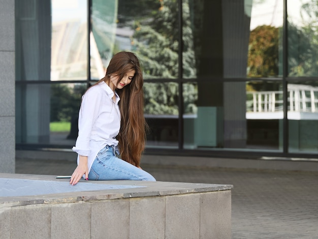 Junge schöne lächelnde Frau mit langen Haaren sitzt allein am Rand der Brüstung