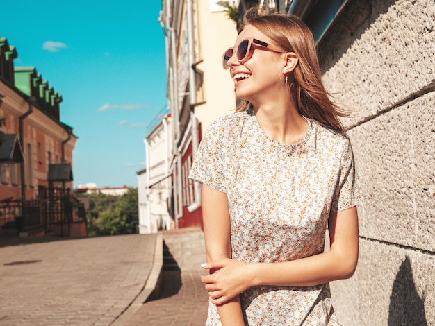 Junge schöne lächelnde Hipster-Frau in trendiger Sommerkleidung Sexy sorglose Frau, die bei Sonnenuntergang auf dem Straßenhintergrund posiert Positives Modell im Freien Fröhlich und glücklich mit Sonnenbrille