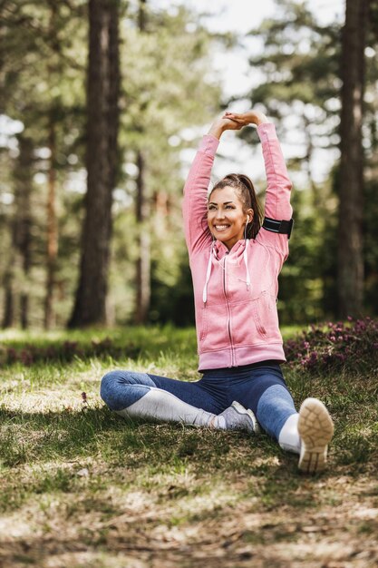 Junge schöne lächelnde Läuferin, die sich nach dem Joggen in der Natur ausdehnt.